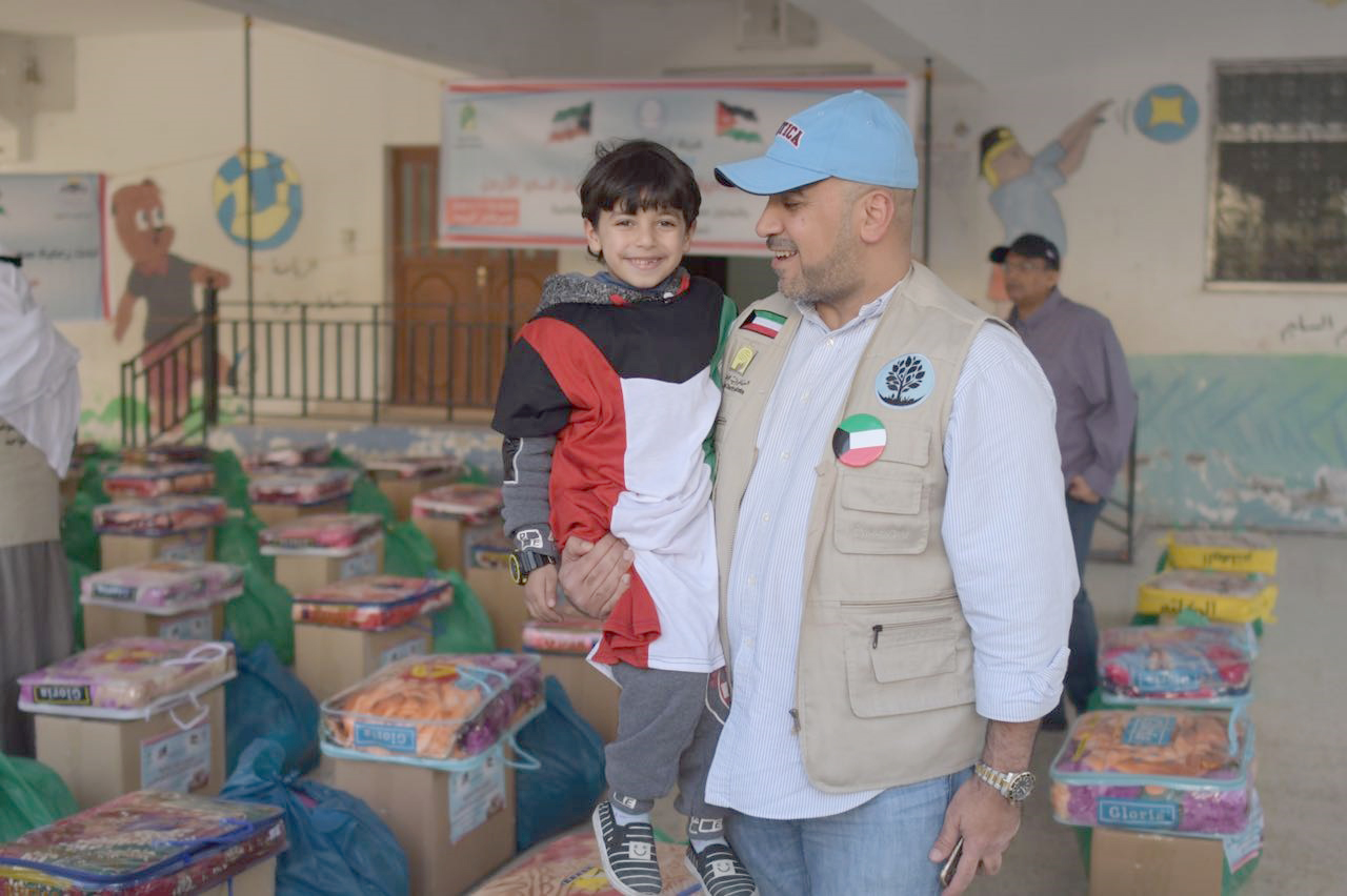 عضو فريق (تراحم) التطوعي يحمل احد الأطفال السوريين خلال حفل توزيع المساعدات على عدد من الأسر السورية